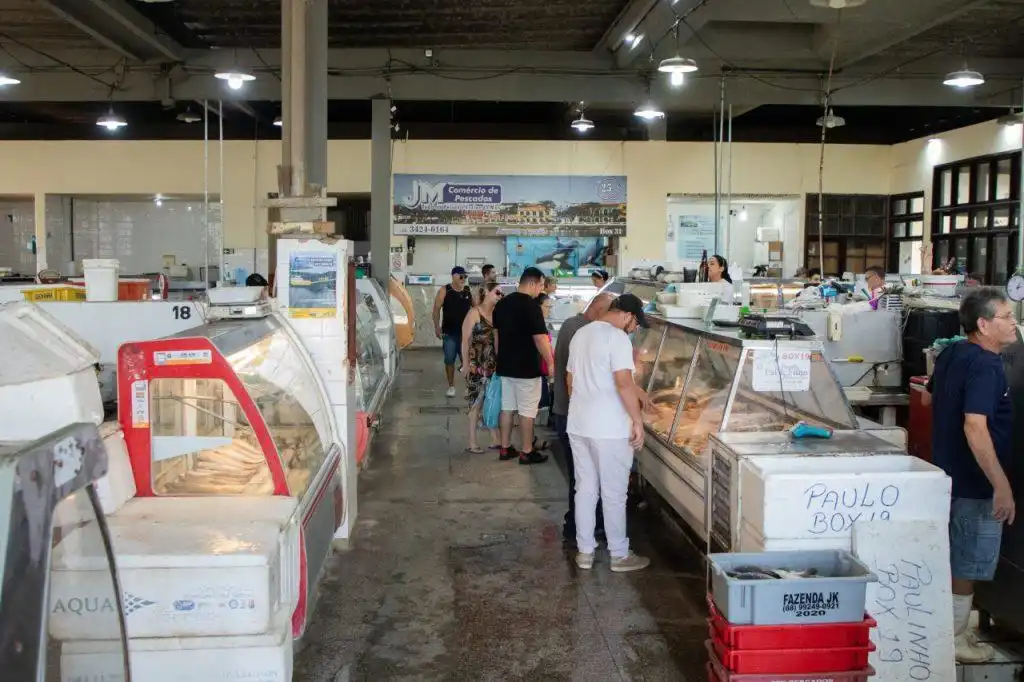 People browse seafood at a bustling indoor fish market, with various stalls displaying fresh catches under bright lighting