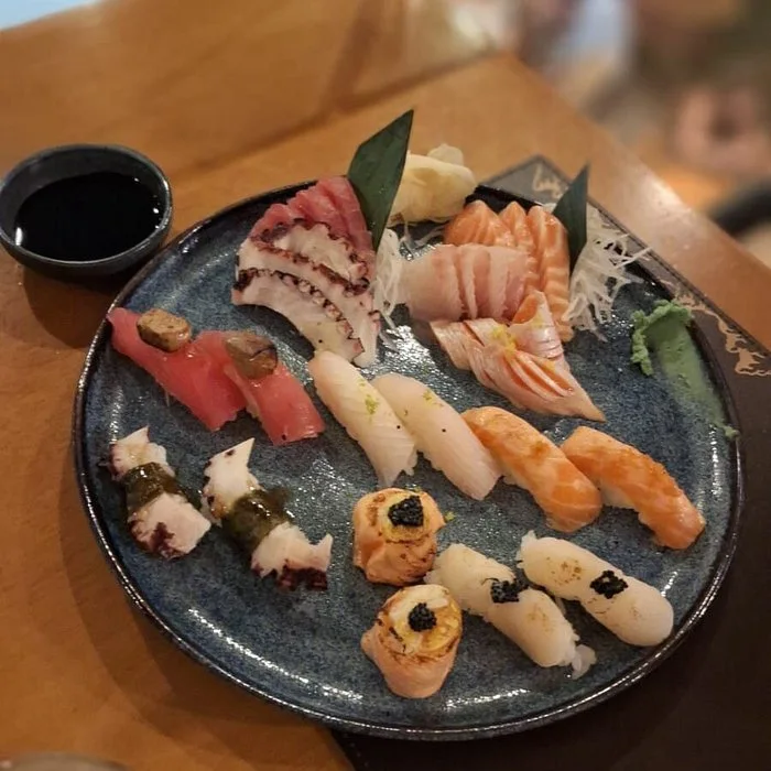 A blue plate with assorted sushi and sashimi, including salmon, tuna, and octopus, served with wasabi and soy sauce on the side.