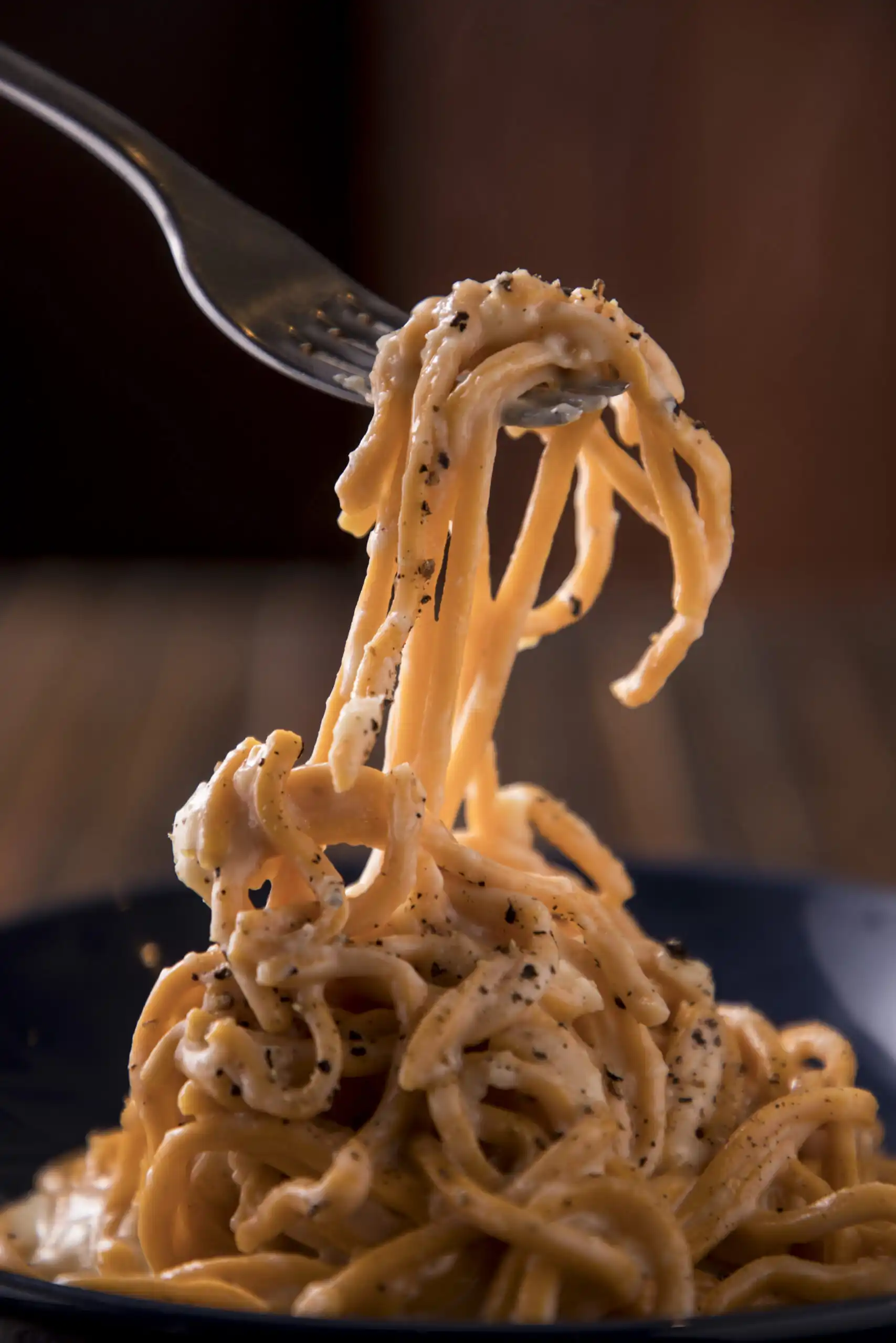 A fork twirls creamy spaghetti with black pepper, highlighting the rich texture and savory aroma against a warm, blurred background.