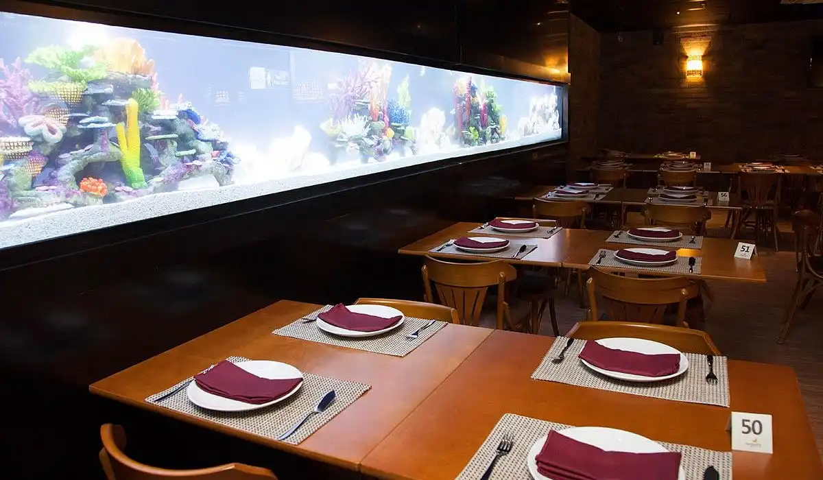 A restaurant with wooden tables set for dining, featuring a vibrant, long aquarium along the wall, creating a cozy ambiance.