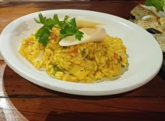 A white plate with yellow rice, garnished with parsley and slices of cheese, sits on a wooden table, ready to be served.
