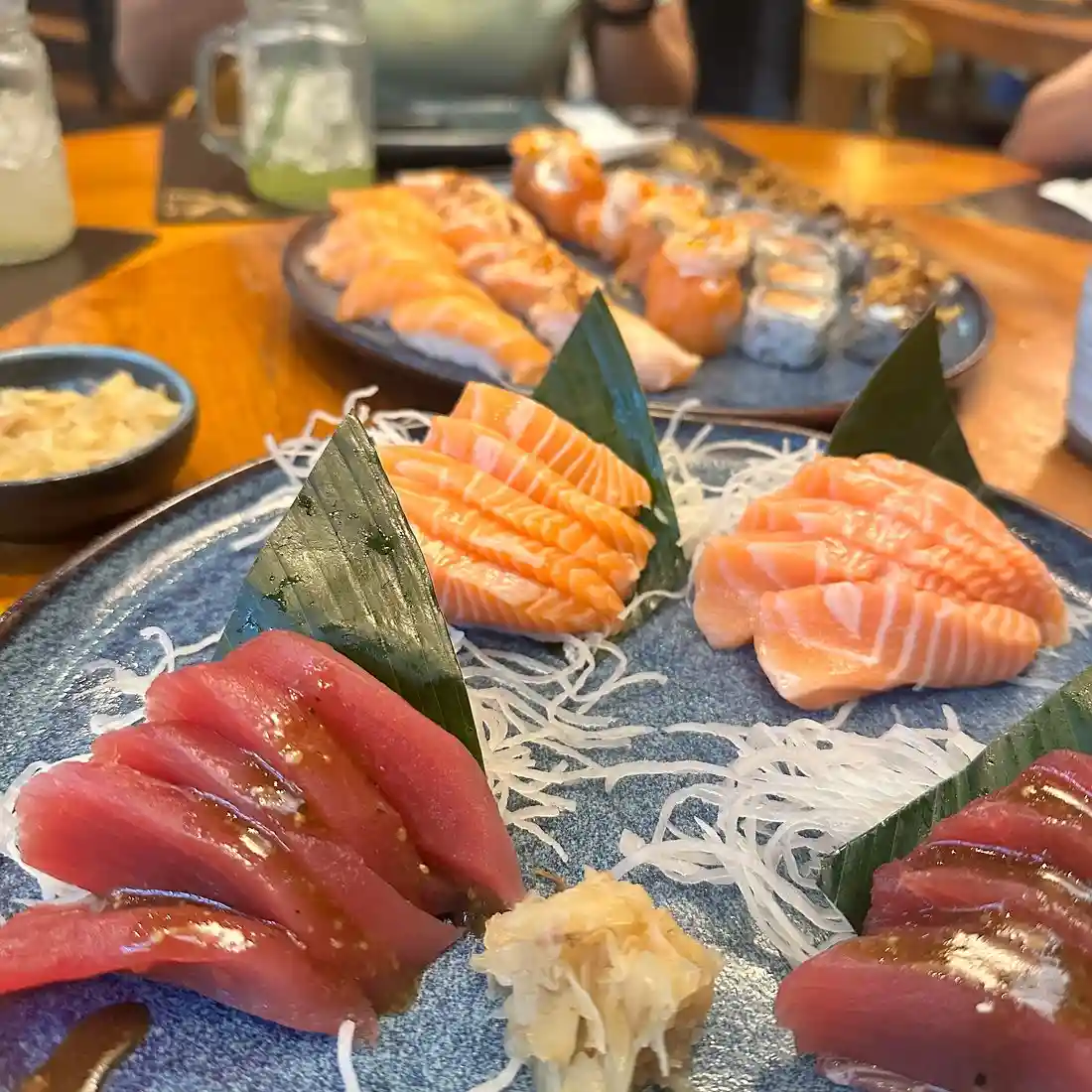 Close-up of assorted sashimi on a blue plate, featuring salmon and tuna slices, garnished with wasabi and ginger.