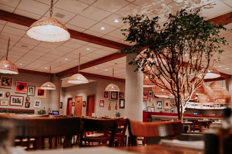 Cozy restaurant interior with wooden chairs, warm lighting, wall art, and a large indoor tree creating an inviting atmosphere.