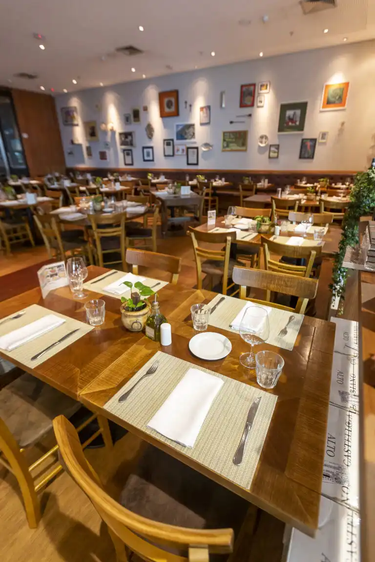 Cozy restaurant with wooden tables set for dining, surrounded by framed art on walls, creating a warm, inviting atmosphere.