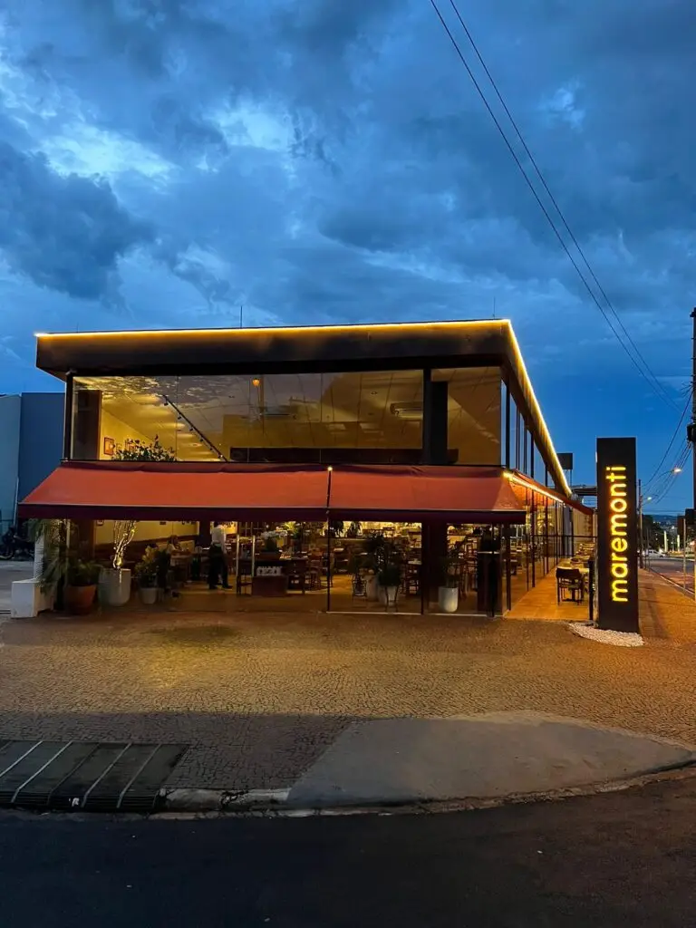 Modern restaurant with red awning and glowing maremonti sign, set against a dramatic evening sky.