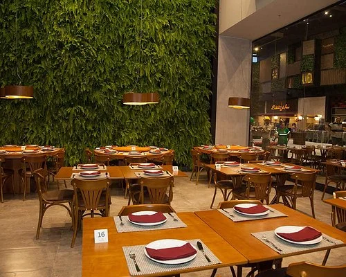 Modern restaurant with wooden tables, red and white plates, and a lush green wall, creating a cozy and inviting atmosphere.
