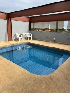A private, rectangular swimming pool on an outdoor terrace, lined with bright blue square mosaic tiles, flanked by a small white table and two chairs against a gray wall with a red steel frame.