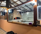 Wood-fired brick pizza oven with glowing fire, viewed through a large glass partition inside a restaurant with a wooden roof structure.