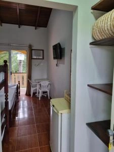 Interior view of a small, tiled guest room showing a wooden bunk bed, a white mini-fridge, wall-mounted shelving, and a small white dining table. In the background, glass sliding doors open to a sunny outdoor balcony.