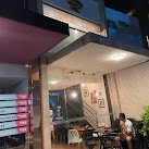 Nighttime modern restaurant storefront with red awning, glass facade, and outdoor bistro seating.