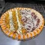 Round pizza on metal tray divided into two halves; one side with meat and onions, the other with cheese and yellow toppings.