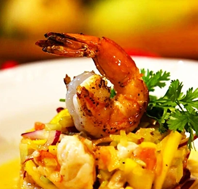 Macro shot of a seasoned grilled shrimp perched on a bed of diced citrus and vegetable salad, garnished with fresh parsley.