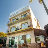 Modern, three-story pousada hotel facade featuring floor-to-ceiling glass doors, balconies, and white stone accents, located steps away from the beach.