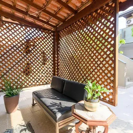 A shaded outdoor seating area featuring a wooden lattice privacy wall, a gray outdoor sofa, and a small hexagonal side table with potted green plants on a light tile floor.