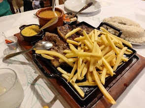Cast-iron sizzling steak platter with french fries, side bowls of yellow rice, beans, and sauces.
