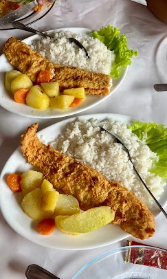 Two plates of breaded baked fish fillets served with white rice, boiled potatoes, carrots, and fresh lettuce on a white tablecloth.