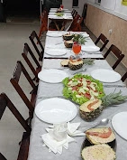 Long dining table set with white plates, fruit salad on lettuce, hollowed-out pineapple bowls, and an orange beverage in a glass.