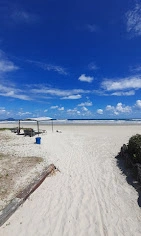 Expansive, empty white sandy beach with a perfect bright blue sky and fluffy clouds, featuring a rustic beach umbrella and calm ocean waves in the distance.