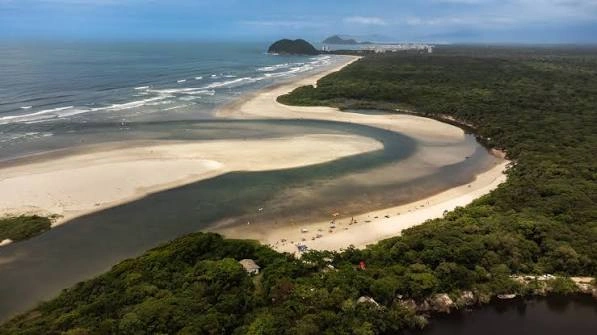 Overhead shot of the Meandering river flowing into the ocean, creating a large expanse of white sand at Itaguaré, surrounded by dense green tropical forest with tiny people relaxing on the beach.