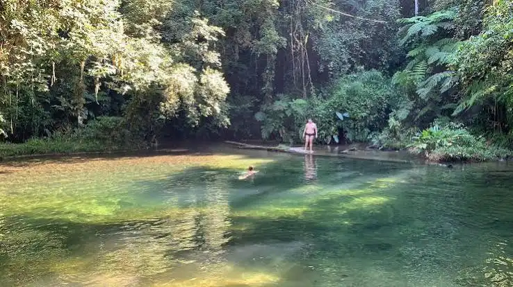 A split image showing two views of Poço do Limão: on the left, a rustic wooden archway with the name "Poço do Limão" marking the entrance to a tranquil pool; on the right, a small waterfall cascading over smooth rocks into a clear pool, bordered by a bamboo observation walkway.