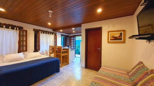 Cozy holiday apartment interior featuring a bed with blue sheets, a colorful striped sofa, a wooden dining table for two, and an open doorway leading to a private patio.