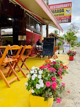 Outdoor restaurant patio with bright yellow floor, wooden chairs, chalkboard menu, and flower pots.
