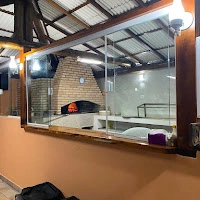 Interior view of a commercial kitchen featuring a brick pizza oven with active fire, enclosed behind a glass wall and wooden frame.