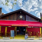 Wooden A-frame restaurant exterior with central clock, bright red awning, and yellow paved entrance.