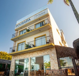 Spacious family hotel room designed with white walls, a prominent teal accent panel, and light wood-laminate flooring. The room includes a main double bed with a green runner, a single twin bed, a wall-mounted air conditioner, and sliding glass doors leading to a sunny balcony.