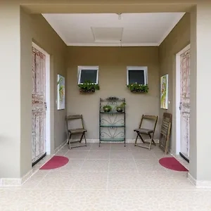 A bright tiled interior entrance area with two distressed white wooden doors, small floral window boxes, metal folding chairs, and a decorative metal tiered plant stand.
