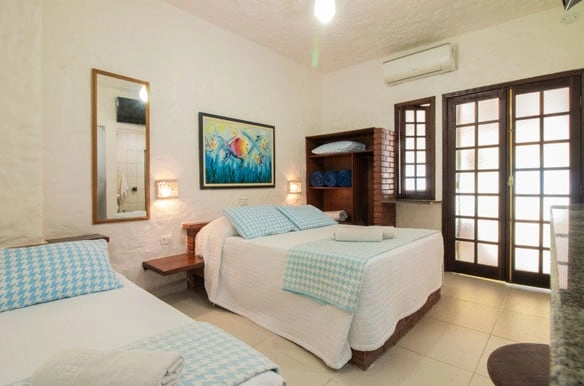 Cheerful bedroom with a large bed, blue-and-white checkered bedspread, a rustic wooden bookcase, and vibrant tropical artwork on the white wall.