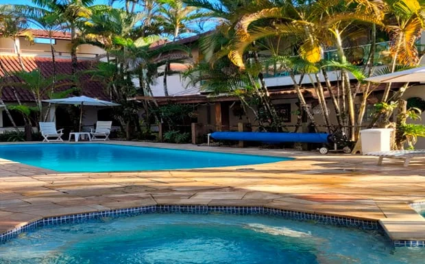 Resort-style swimming pool with sparkling blue water, surrounded by stone decking and towering mature palm trees under a clear blue sky.
