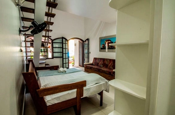 Bright and airy bedroom with a wooden bed frame, floor-to-ceiling glass doors leading to the patio, and a comfortable brown leather sofa.