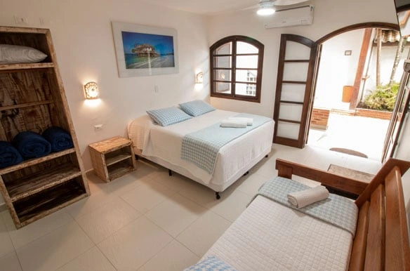 Comfortable guest bedroom with a double bed, blue patterned throws, a rustic wooden shelving unit for towels, and a scenic beach photo on the wall.