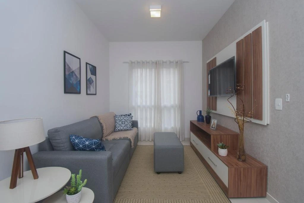 Contemporary living room featuring a grey sofa with blue patterned pillows, a grey ottoman, a wooden media console, and a mounted TV against a textured grey wall.