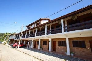 Low-angle view of a two-story brick lodge building with white pillars, a wooden balcony, and a red truck parked on a cobblestone street under a bright blue sky.