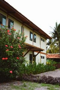 Low-angle view of a two-story building with cream walls, wooden structural beams, a tiled roof, and glass windows, featuring a large hibiscus bush with red flowers in the foreground.