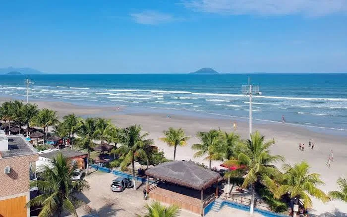 Aerial view of a coastal town nestled between lush green tropical forest and a long crescent beach with turquoise ocean waters.