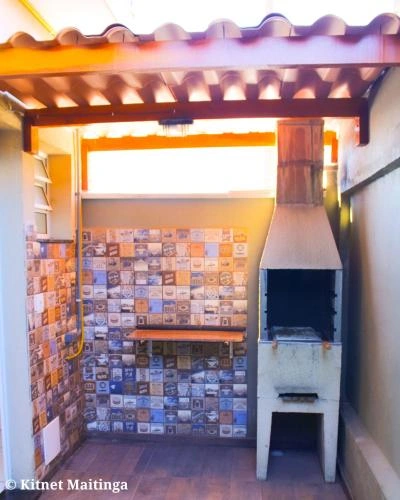 Rustic covered outdoor churrasqueira area with colorful tiled walls, a wooden counter, and a built-in brick barbecue grill.