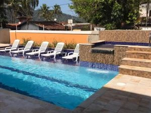 Outdoor view of a blue-tiled swimming pool with a water feature, lined with white sun loungers against a bright orange wall under a clear sunny sky.