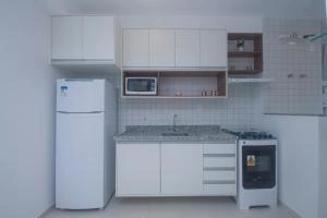 Functional white kitchen featuring upper and lower cabinets, a white refrigerator, granite countertops, a built-in microwave, and a stove.