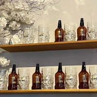 Wooden shelves displaying amber beer bottles and mugs next to white floral decorative branches.