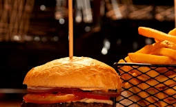 Juicy beef burger with tomato and onions, secured with a skewer, served alongside crispy fries in a wire basket.
