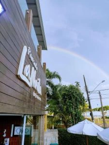 Close-up of the rustic wooden Pousada La Naila hotel sign under a blue sky with a visible rainbow in the background.