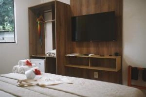 Interior view of a bedroom featuring a large wooden wall unit with a mounted flat-screen TV, open shelving, a mini-fridge, and a bed with white towels and red flower decorations.