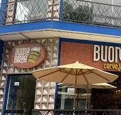 Daytime view of the Buona Birra restaurant facade with a round "Cerveja" logo and umbrellas.