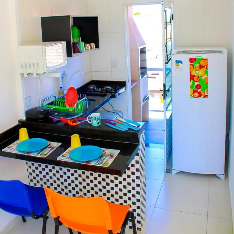 Bright and compact kitchenette with black countertops, a black-and-white checkered island, white fridge with fruit decal, and two colorful bar stools.