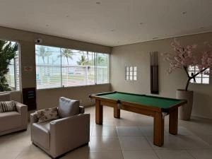 Spacious entertainment lounge featuring a green felt pool table, white armchairs, a large window with scenic views, and a decorative faux cherry blossom tree.