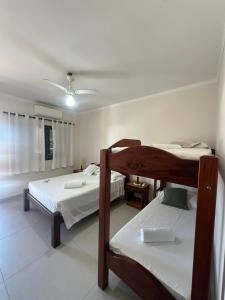 Interior view of a guest room featuring a wooden bunk bed, a separate single bed with white linens, air conditioning, and a ceiling fan.