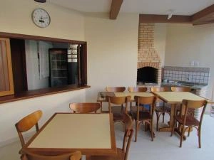 Interior view of a rustic dining room featuring wooden tables and chairs, a counter window, and a large brick barbecue grill area in the background.
